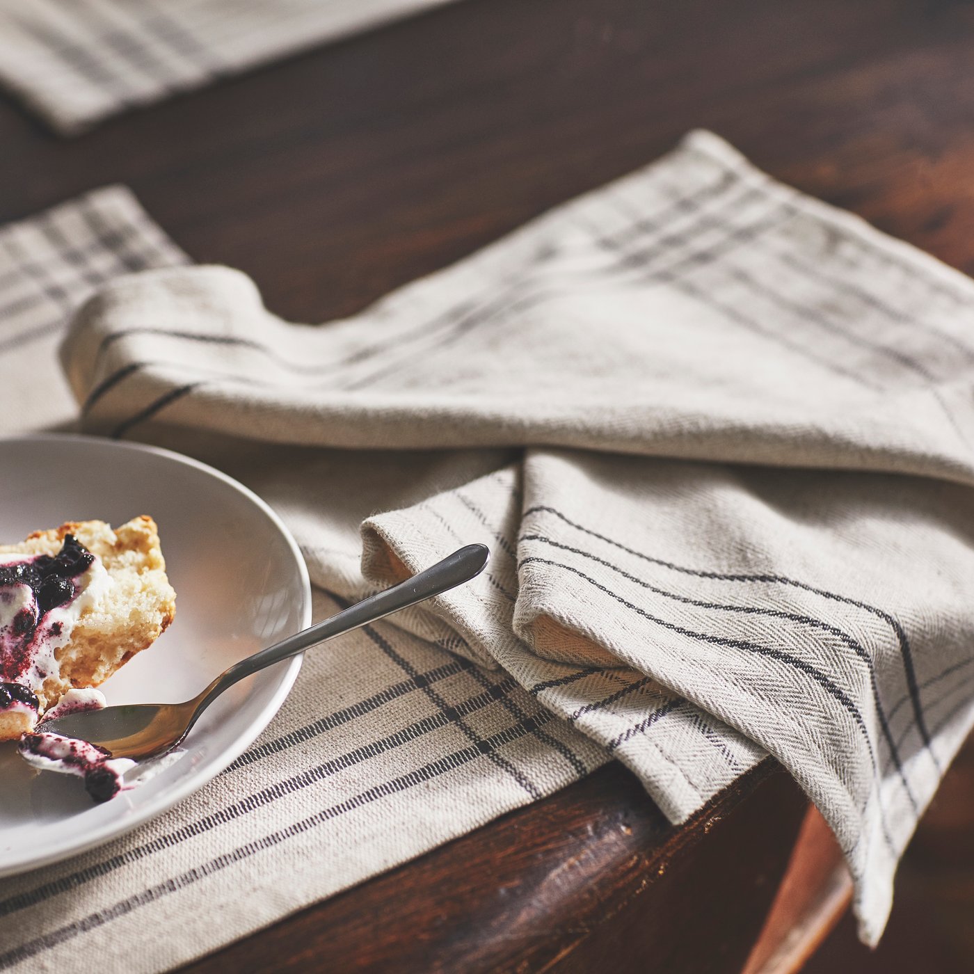  A white plate with croissant and berries on striped linen napkins placed on a dark wooden table.