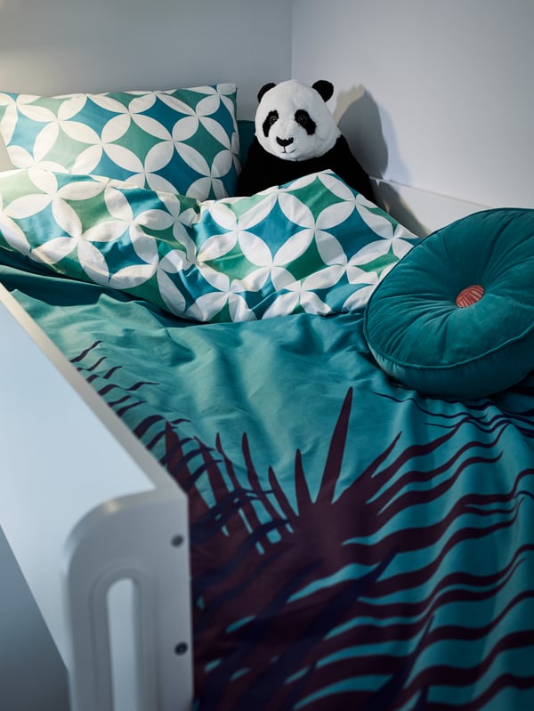 Ein Hochbett mit blau und grün gemusterter Bettwäsche, unter anderem mit einem türkisfarbenen Kissen und einem Stofftier in Form eines Pandabären.