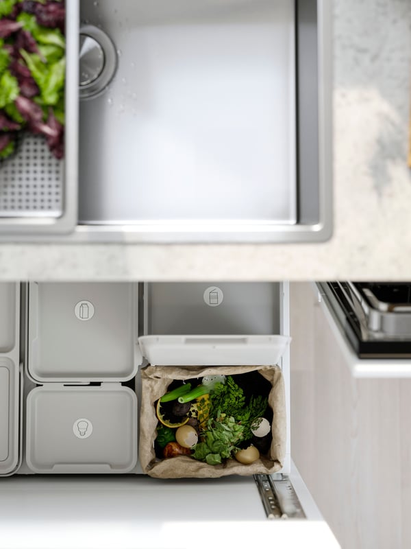 A VRESJÖN inset sink with one bowl has a colander with lettuce in it and waste sorting bins can be seen in the drawer below.