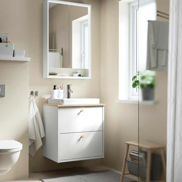 salle de bains HAVBÄCK moderne et bien organisée aux carreaux blancs, munie d’une cabine de douche en verre, d’un meuble avec tiroir en bois HAVBÄCK et divers accessoires pour salle de bains.