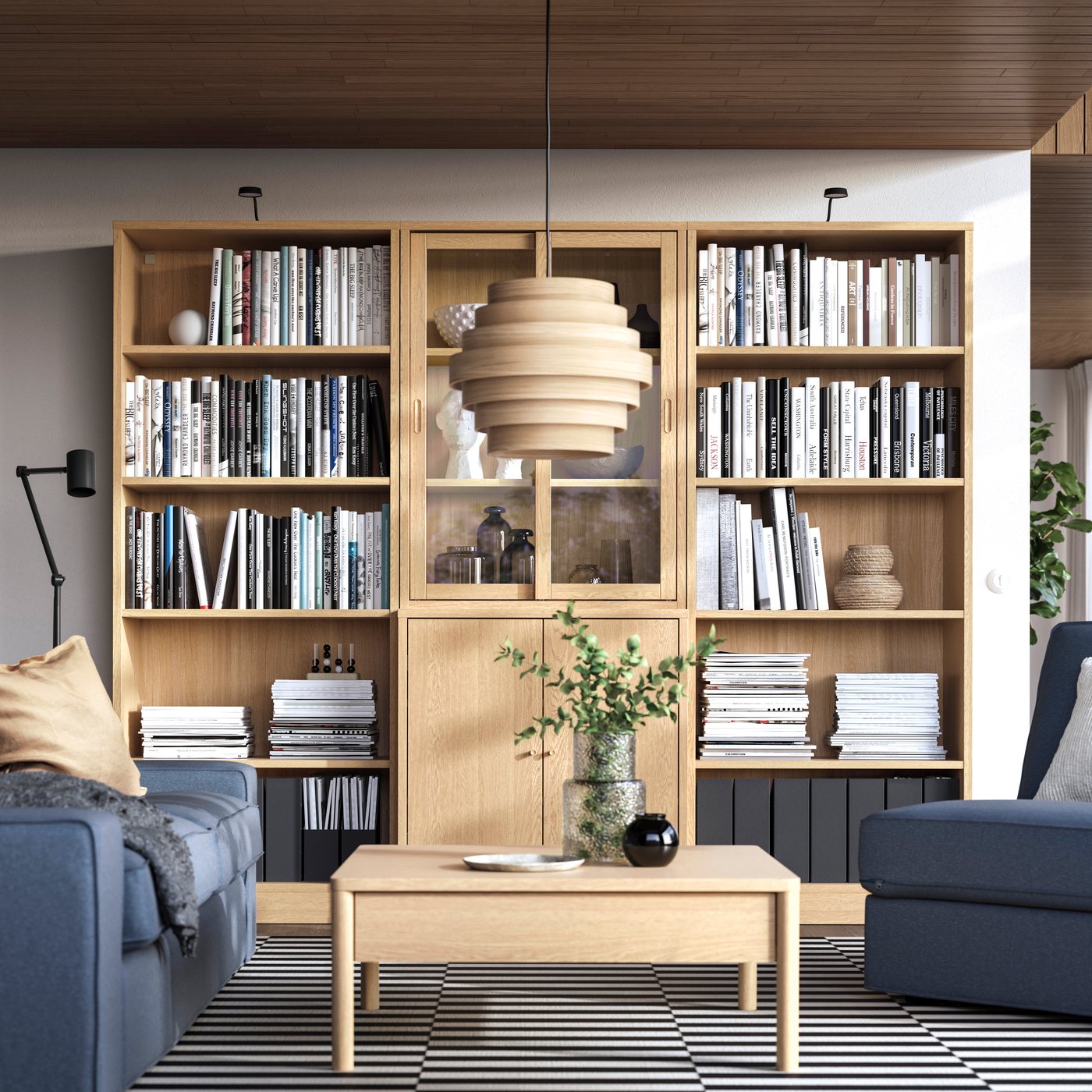 Blick auf ein TONSTAD Wohnzimmerregal mit Büchern in hellem Eicheneffekt mit offenen und geschlossenen Elementen vor dem ein Couchtisch und ein blaues Sofa steht