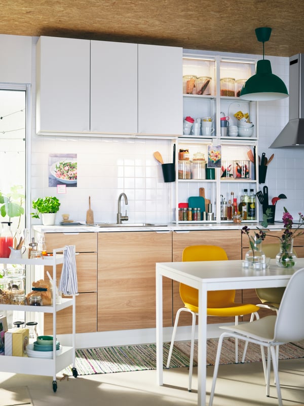 Une cuisine légère avec des rangements ENHET, une table MELLTORP blanche, des chaises de différentes couleurs et une desserte NISSAFORS blanche.