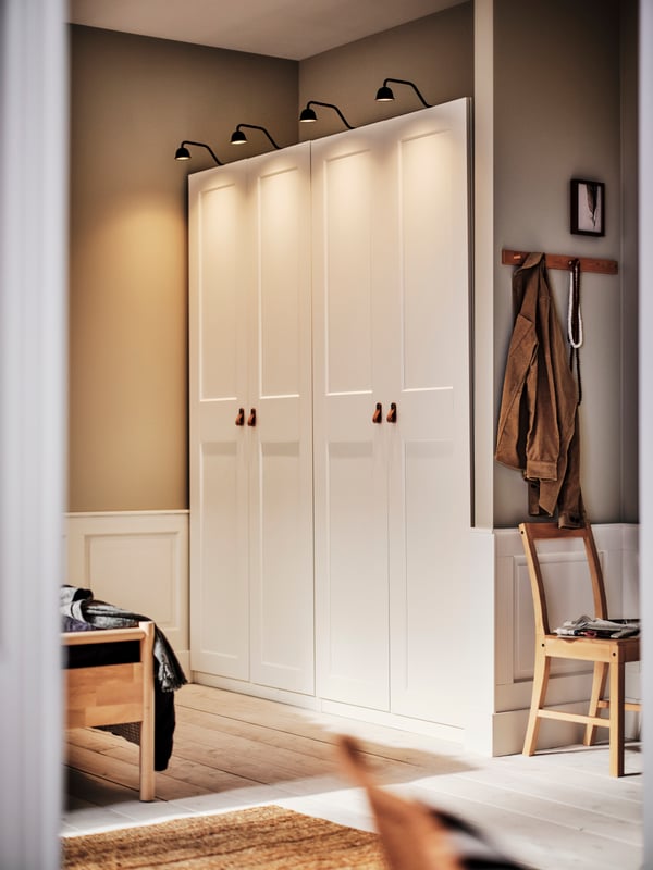 A bedroom with a light brown stained PINNTORP chair, a LOHALS flatwoven rug and two white PAX/GRIMO wardrobes.