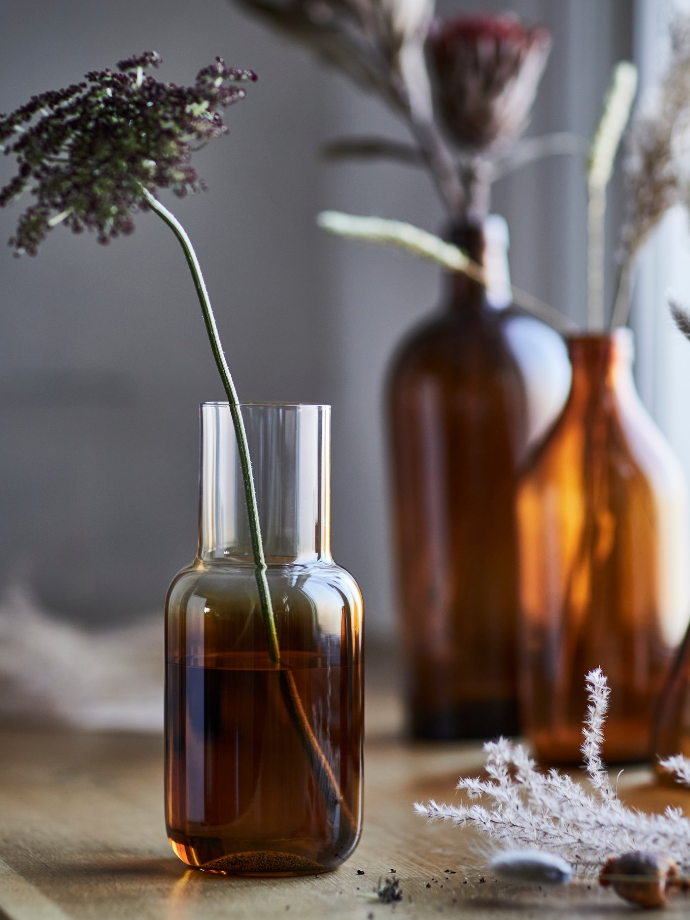 A brown HÖSTAGILLE vase holding a dried flower, elegantly placed on a wooden table with soft ambient light.