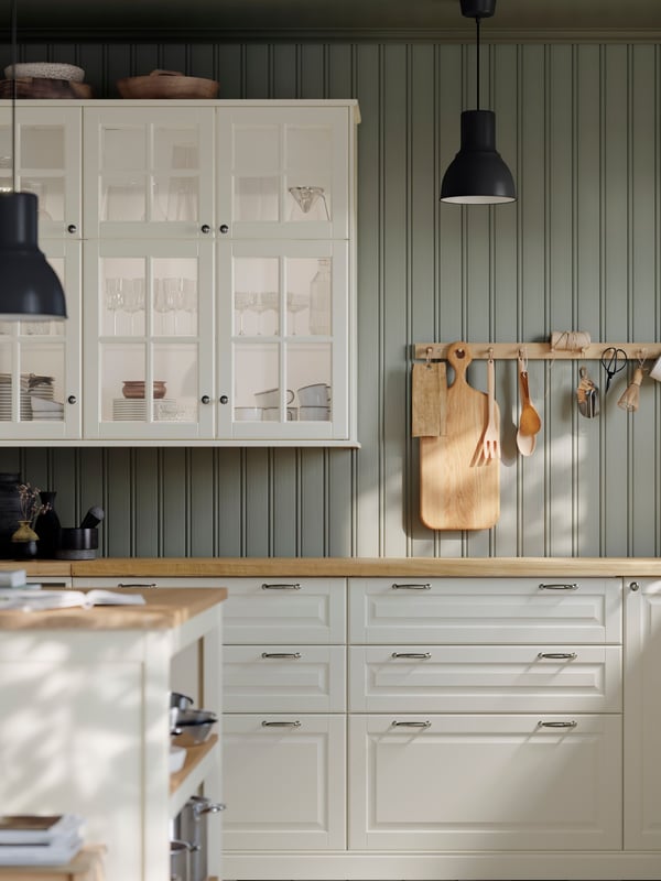Cabinets with BODBYN glass doors in off-white, storage with BODBYN doors in off-white and kitchen items on hooks on the wall.