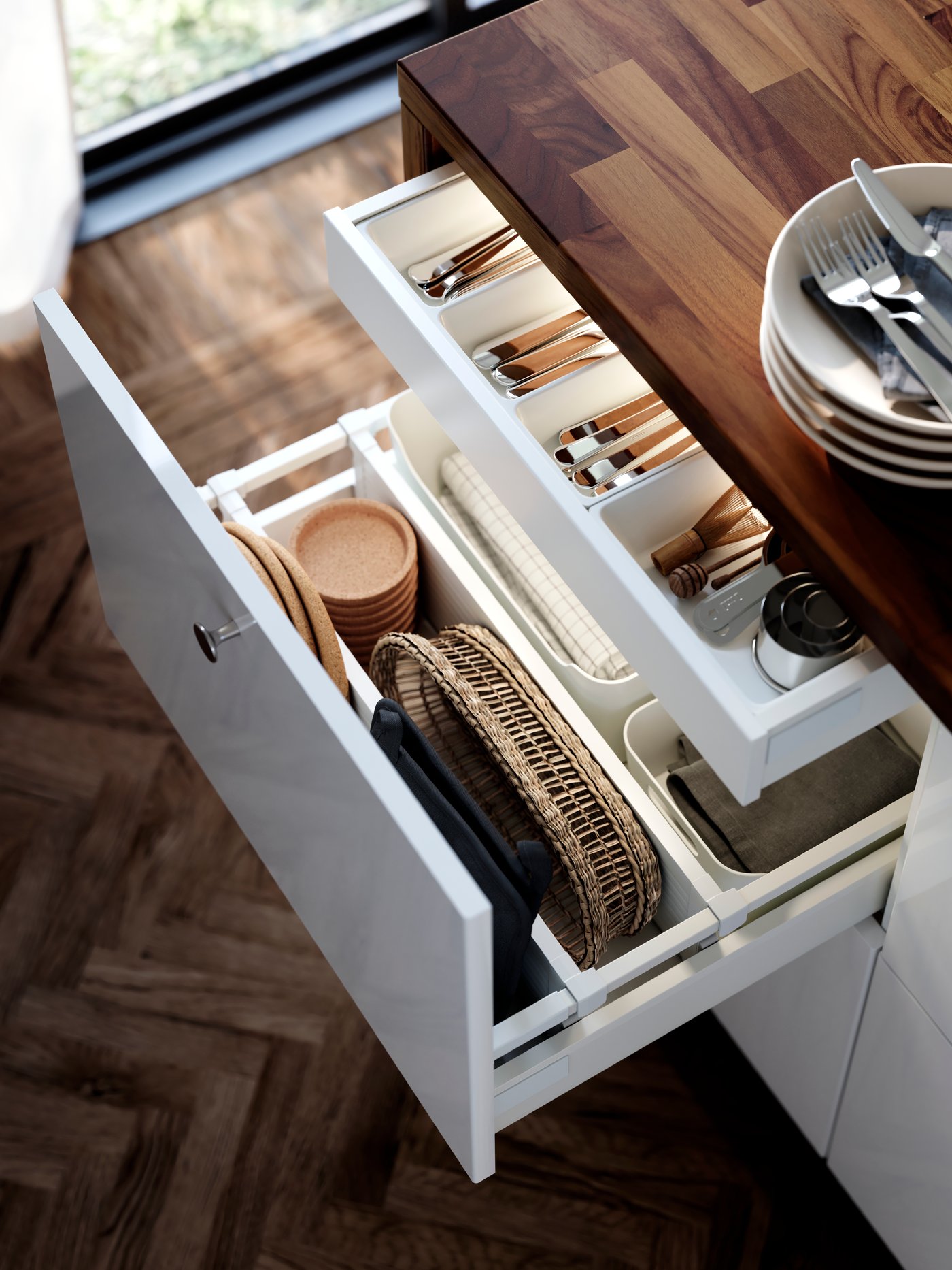 A large drawer in a cabinet with white RINGHULT kitchen fronts is pulled out and there are kitchen items organised inside.