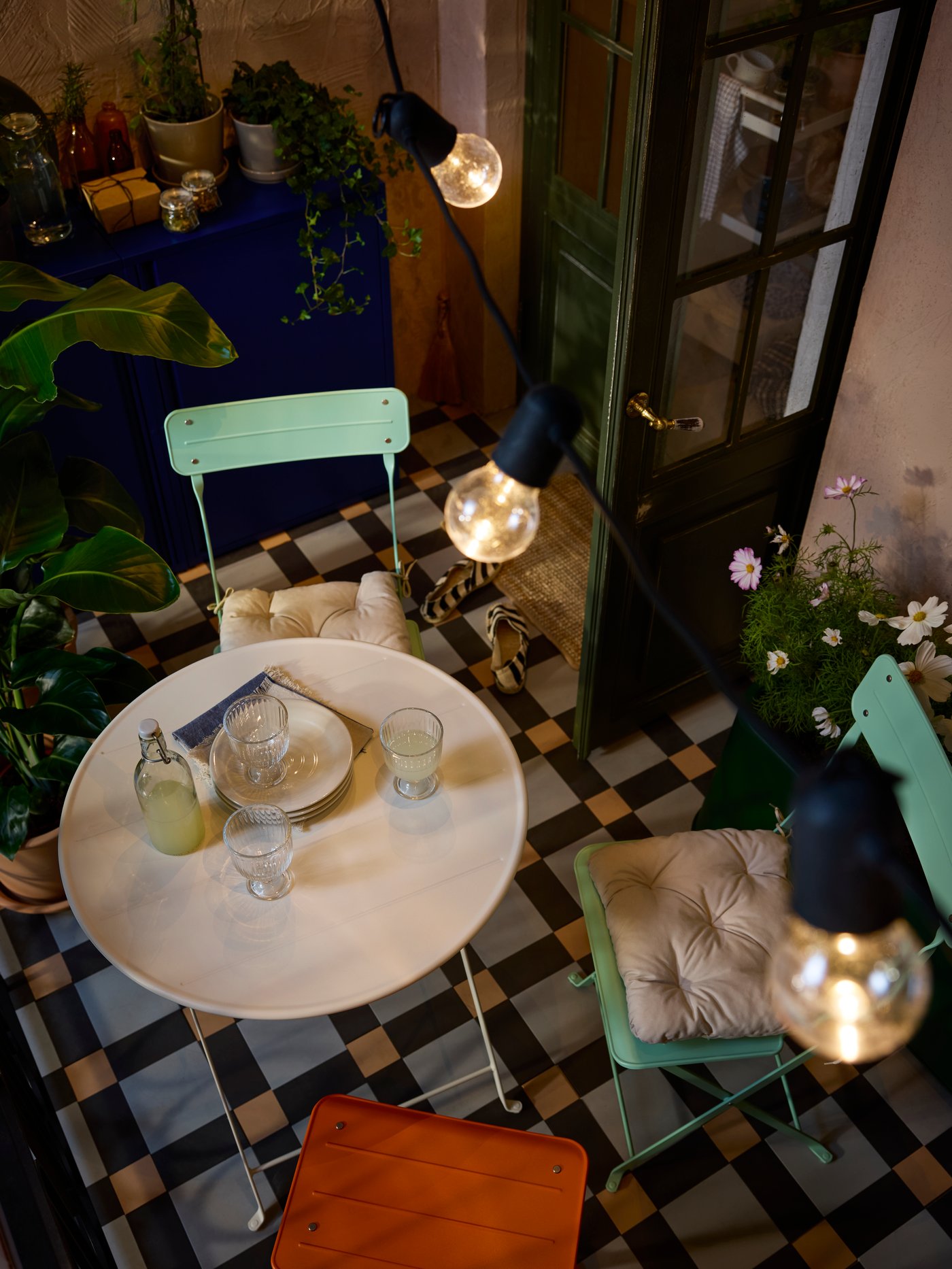 An aerial view of a balcony with SUNDSÖ outdoor table and chairs in playful colours under a SVARTRÅ LED lighting chain.