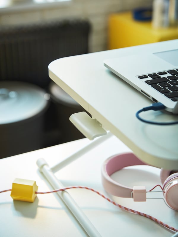 Ein gelber HÅVSKAL USB-Anker hält ein gestreiftes Kabel unter einem Laptop, der auf einem DUBBLA Laptoptisch steht.