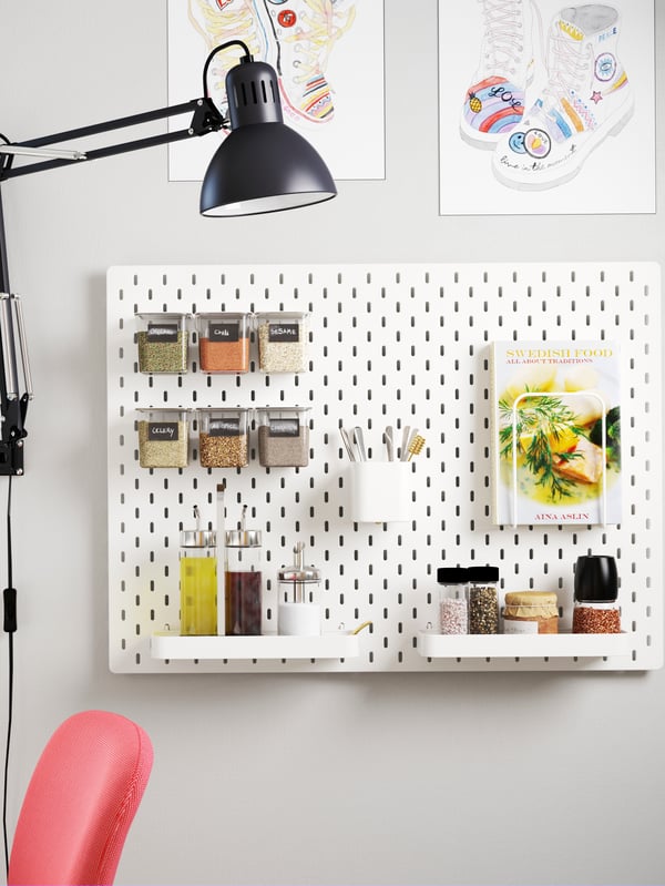 A pegboard mounted on a wall next to a dining table. The pegboard has accessories that store oils, seasonings and a cookbook.