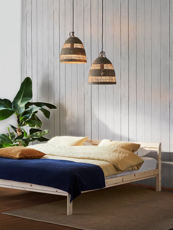Ein niedriges Bett aus unserer NEIDEN Serie steht an einer weißen Wand und darüber hängen 2 Lampen.