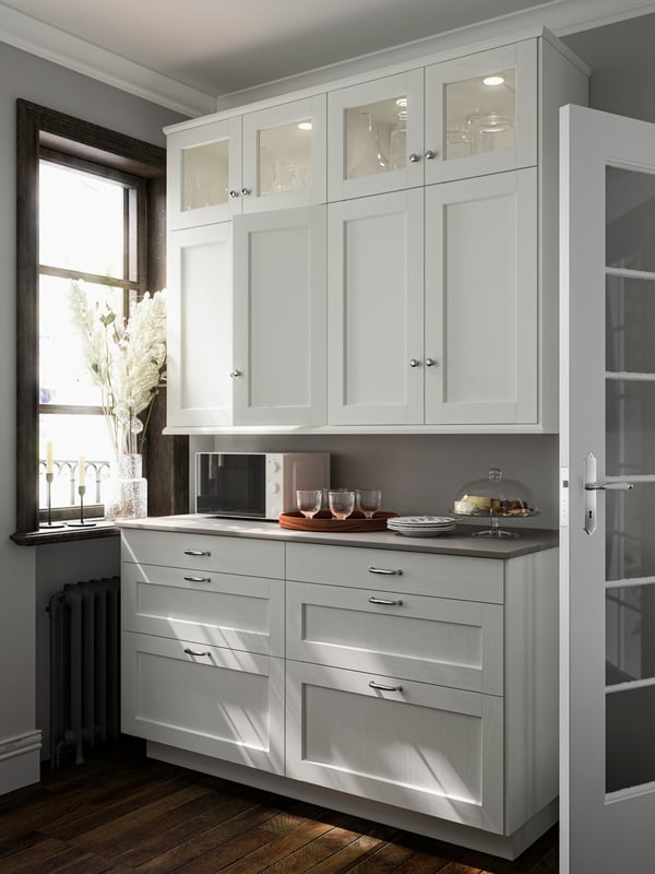 Kitchen cabinets with ENKÖPING doors and cover panels in white wood effect by a window, a microwave and items on the countertop.