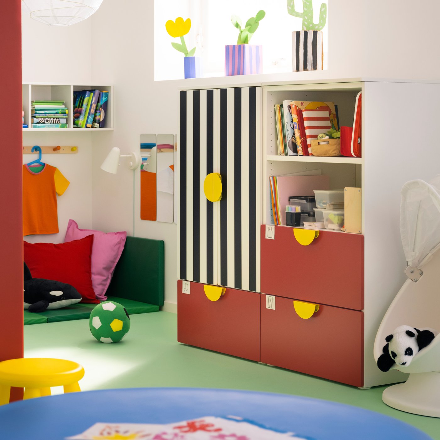 A red and striped SMÅSTAD/PLATSA storage combination with three drawers stands in a child’s room with a green floor.