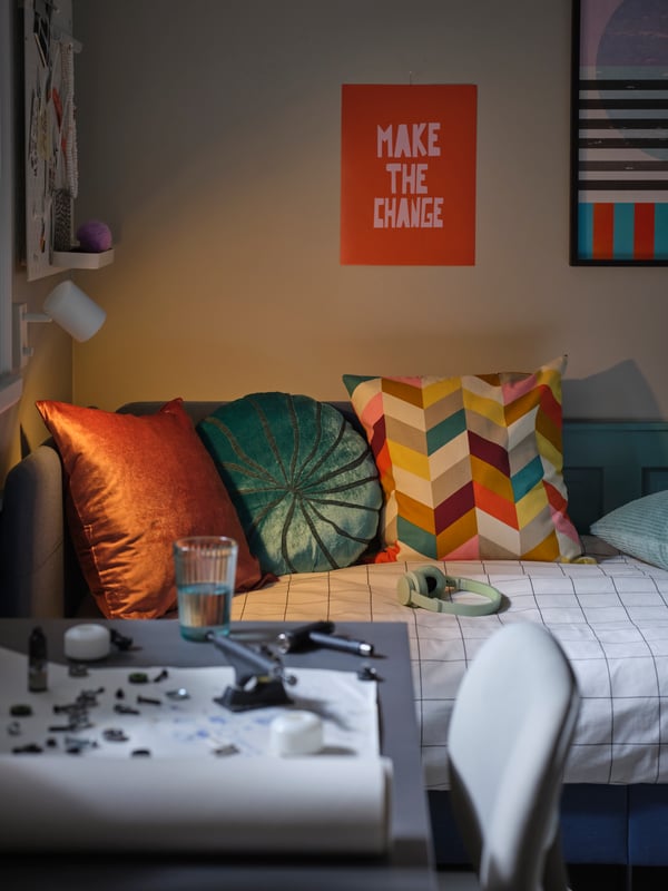 Sur un lit, un coussin dans une housse LAPPVIDE rose, un coussin multicolore HANNELISE et un coussin BLÅVINGAD turquoise.