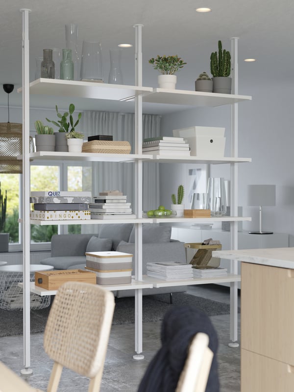 A white shelf system turned room divider between the living and dining areas, with books, games, plants, boxes and more.