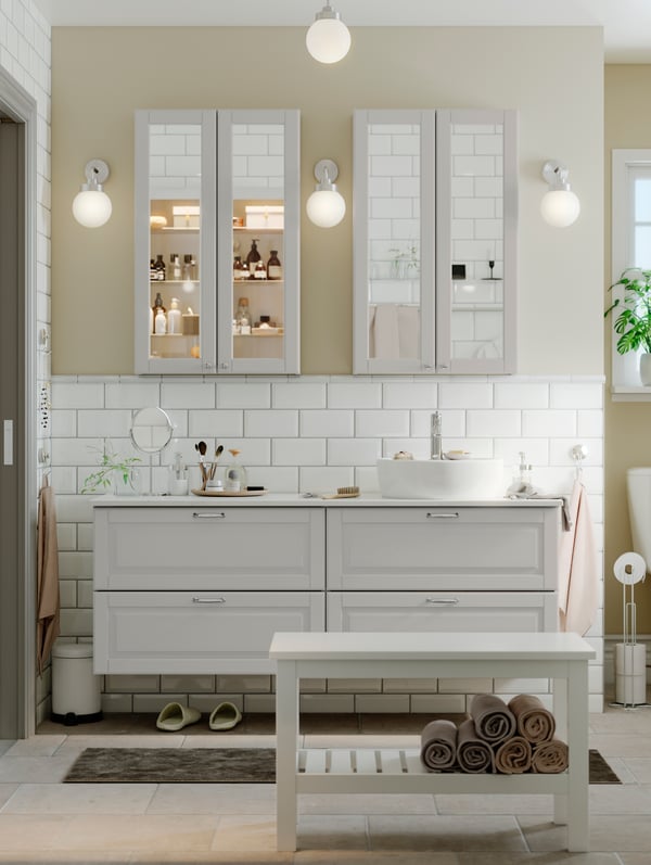 A light-colored bathroom with two wash-stands side by side and two GODMORGON mirror cabinets and three lamps on the wall.