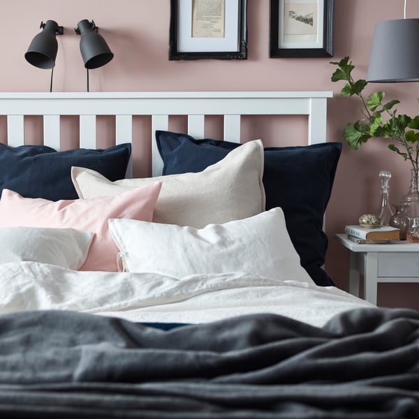 HEMNES white queen-sized bed frame in the bedroom with white, beige, pink and blue cushion covers on top.