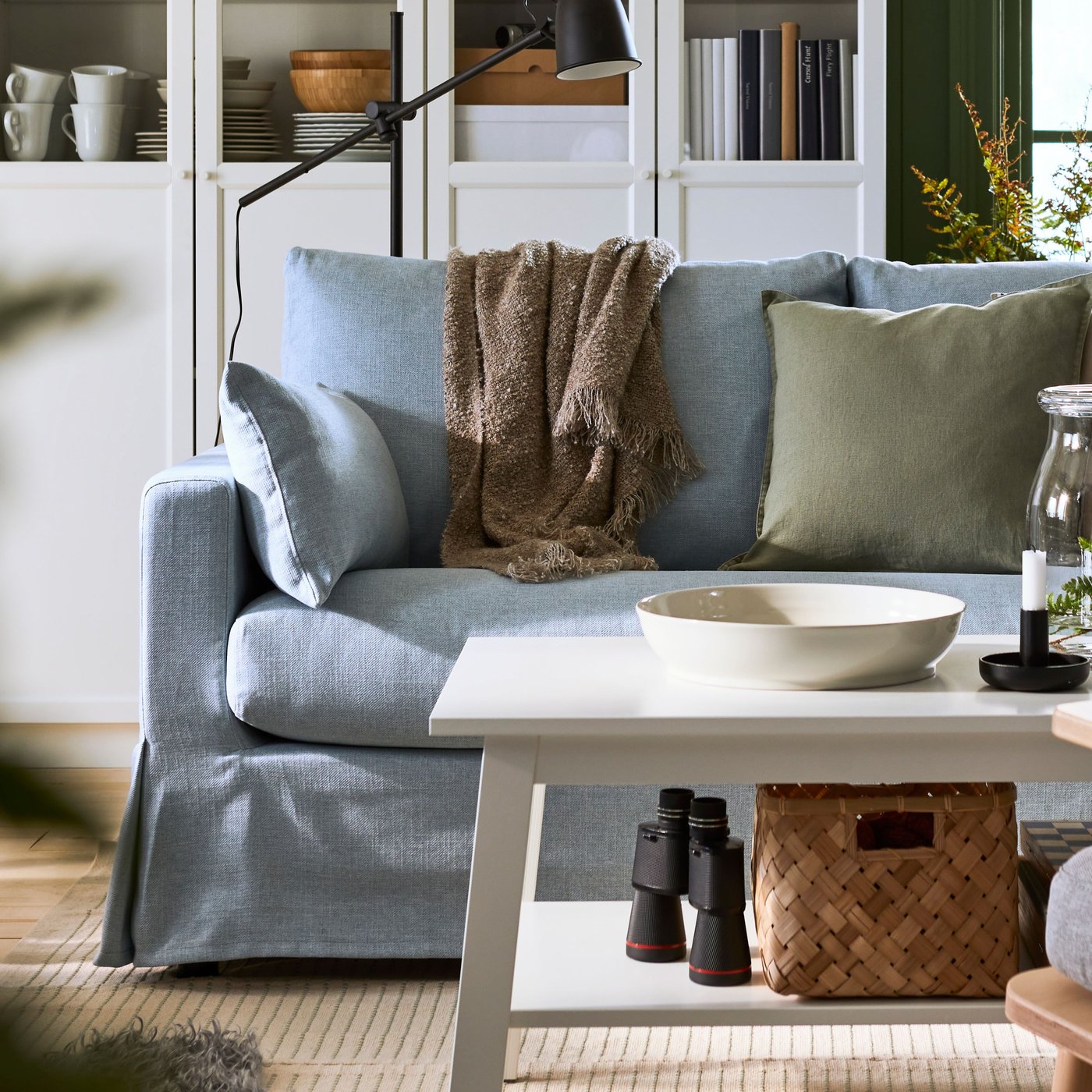 Cosy living room with green walls, a light-blue HYLTARP sofa is placed in front of white BILLY/OXBERG bookcases.