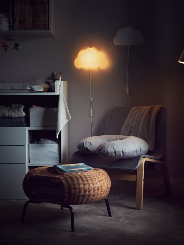 Hämar tuba, mida valgustab pilvekujuline seinalamp, hall tugitool, rotangist GAMLEHULT jalapink, millel toetub padi.