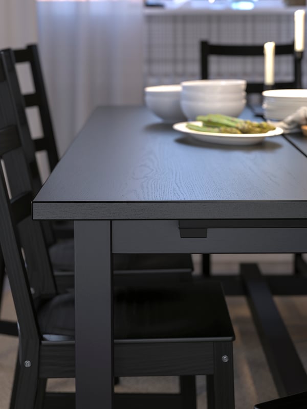 Una mesa negra NORDVIKEN con pocillos blancos pequeños y un plato de espárragos, con sillas negras alrededor.