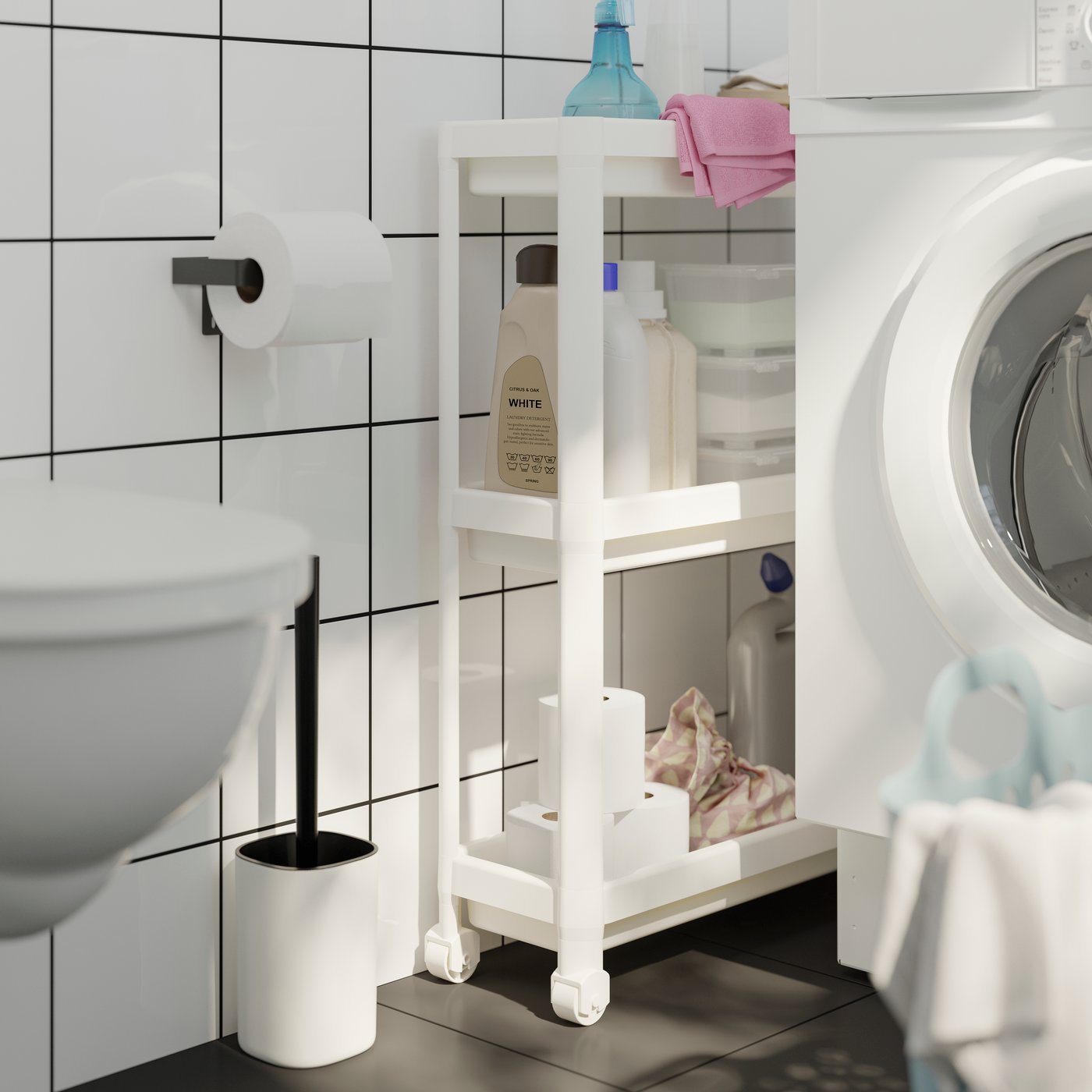 Et smalt VESKEN rullebord med tre hylder fyldt med rengøringsartikler og toiletpapirruller ved siden af en vaskemaskine.