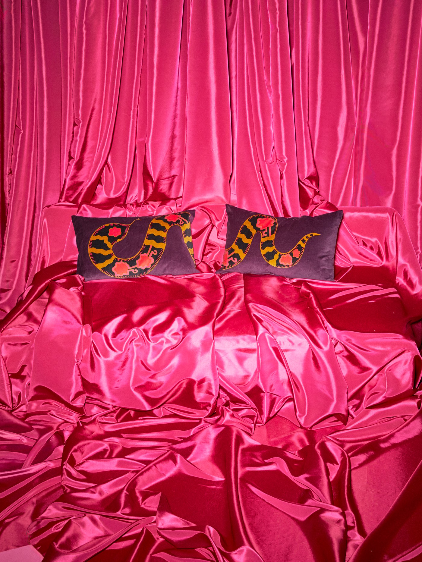 Two purple KARISMATISK cushion covers with snake patterns are on a sofa completely covered in pink satin.