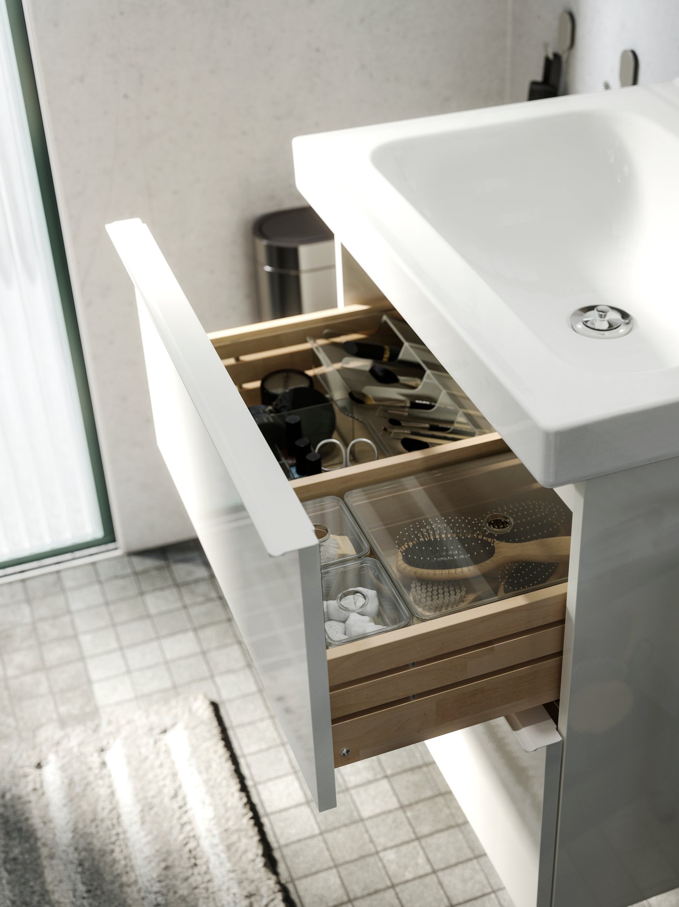 Vanitorio GODMORGON blanco con dos cajones y lavamanos de cerámica ODENSVIK incorporado. El cajón superior está abierto y en su interior se pueden ver cajas organizadoras GODMORGON transparentes con artículos de baño.