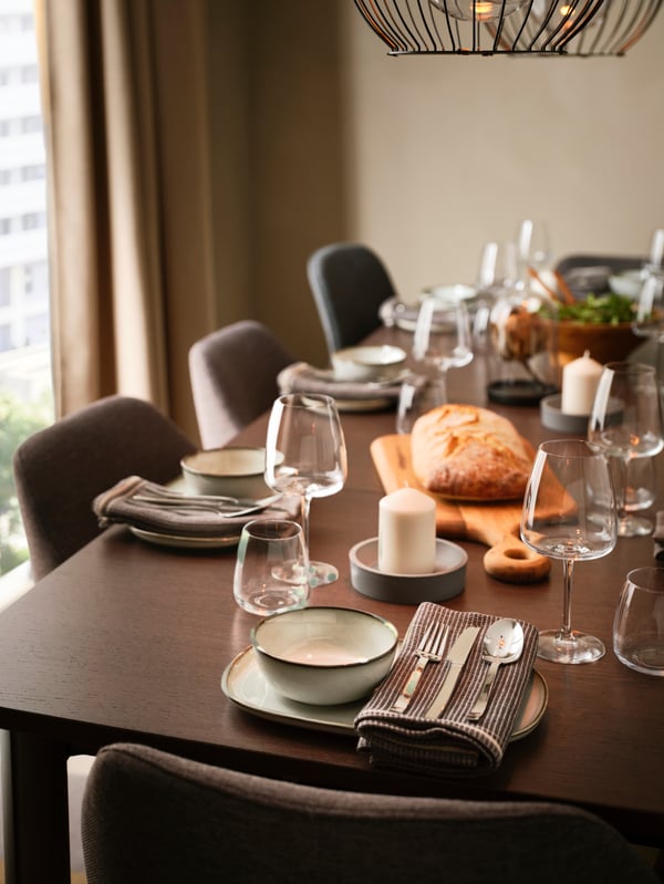 A dining table laid with GLADELIG plates and bowls, with a chopping board in the middle of the table holding a loaf of bread.