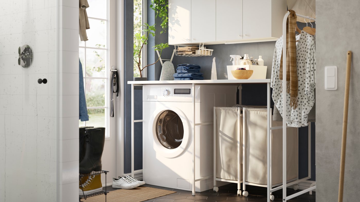 A laundry room with blue walls and a white ENHET storage combination, a washing machine and two laundry baskets on casters.