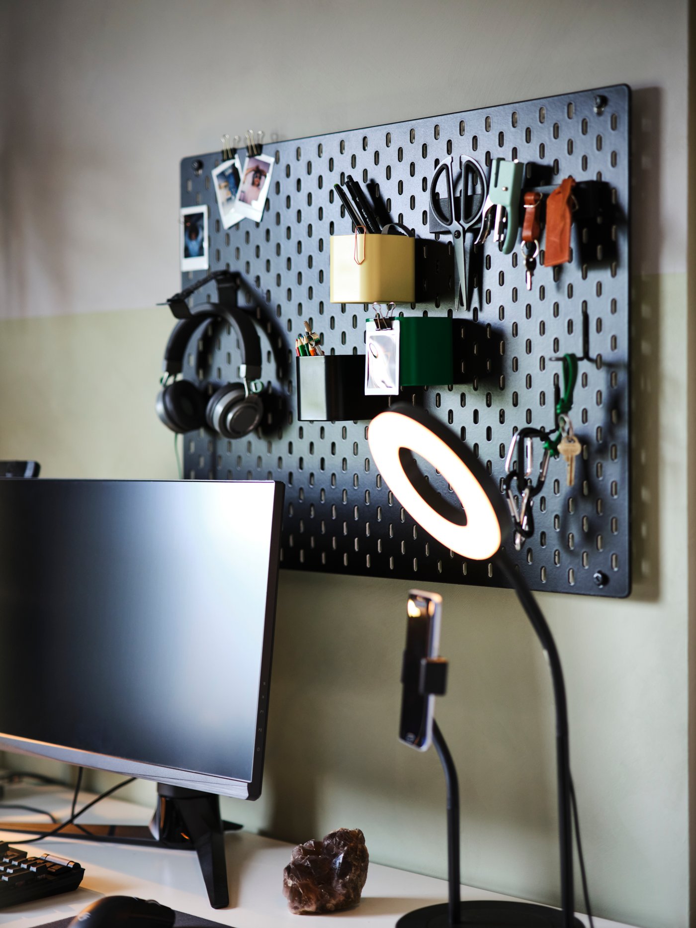 Een zwart SKÅDIS ophangbord is aan de muur bevestigd achter een bureau en een ringlicht. Met deze accessoires vind je snel een plekje voor een pet, sleutelbossen, een schaar, enz.