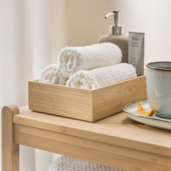 A close-up of a light bamboo STEGESUND box set of 2, holding white towels on a wooden side table.