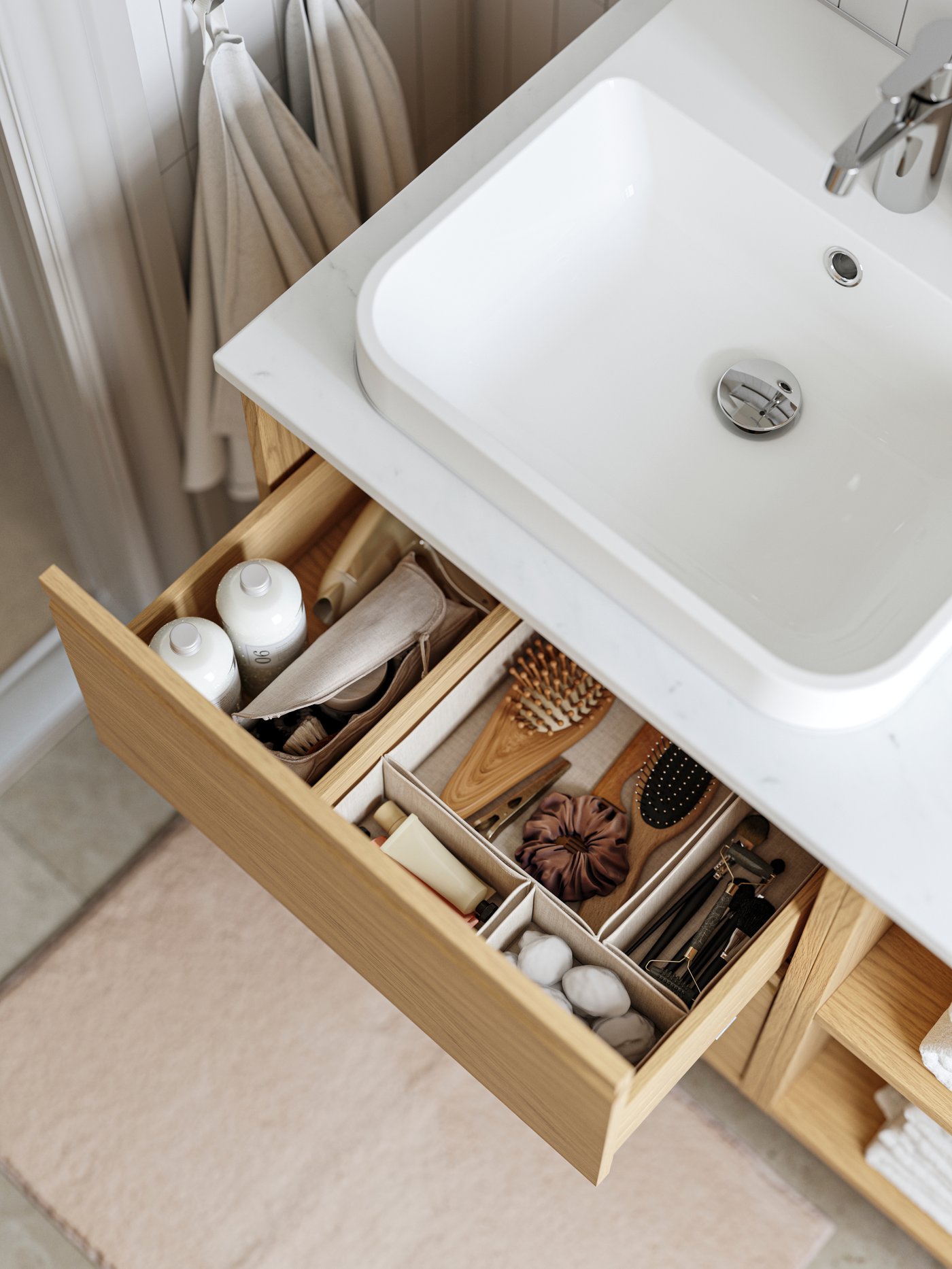 An ÄNGSJÖN vanity with drawers has one drawer pulled out and there are beige BOLLÖSUND drawer organizers inside.