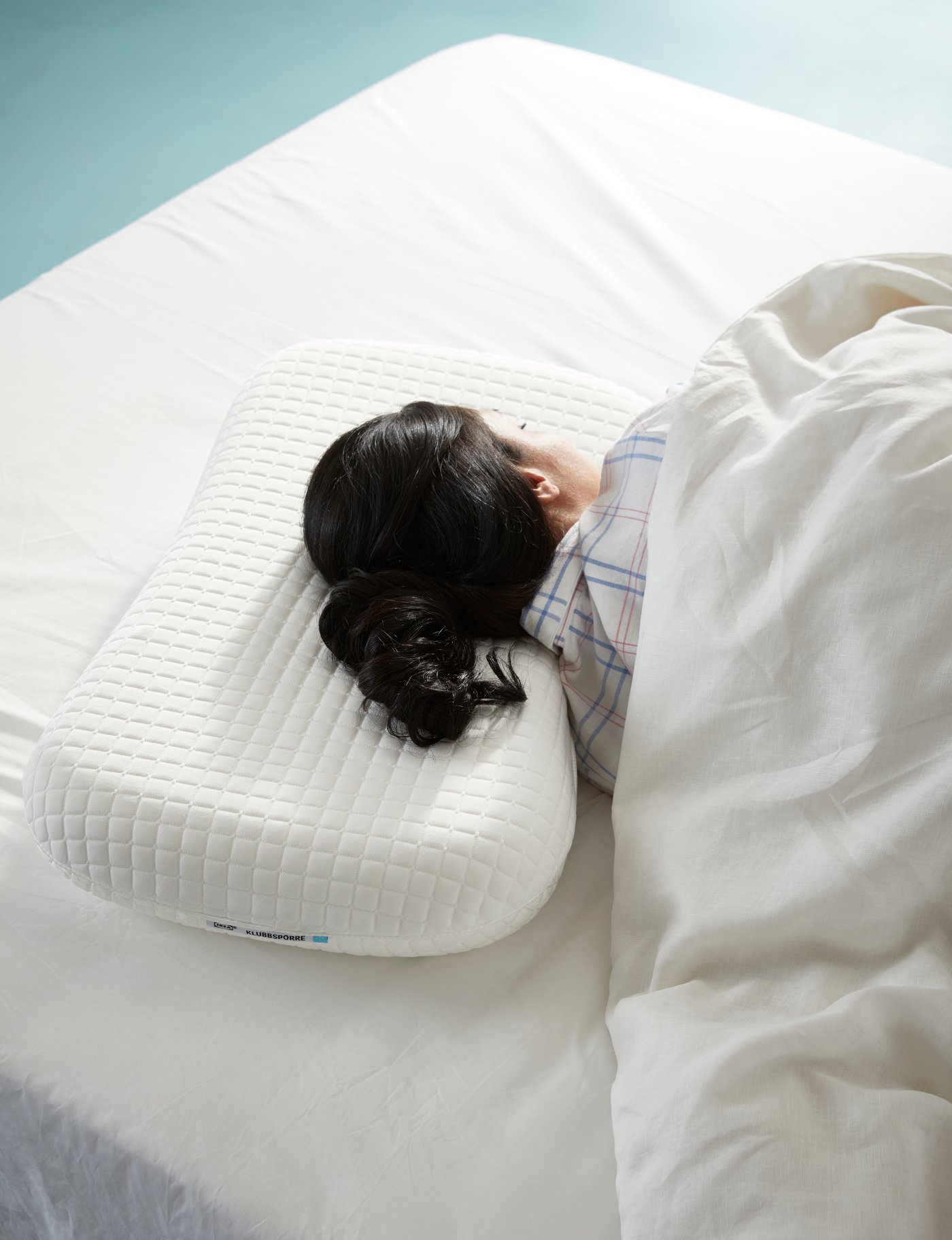 KLUBSPORRE ergonomic memory foam pillow with cooling gel on one side of a mattress with a lady lying on it.