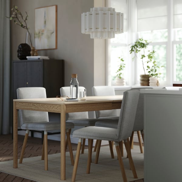Lámpara de techo STOCKHOLM 2025 en blanco textil con detalles chapados en latón, suspendida sobre una mesa de comedor con sillas tapizadas.