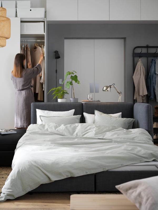 Un canapé-lit VALLENTUNA converti en lit deux places avec couette et oreillers, et une femme en arrière-plan.