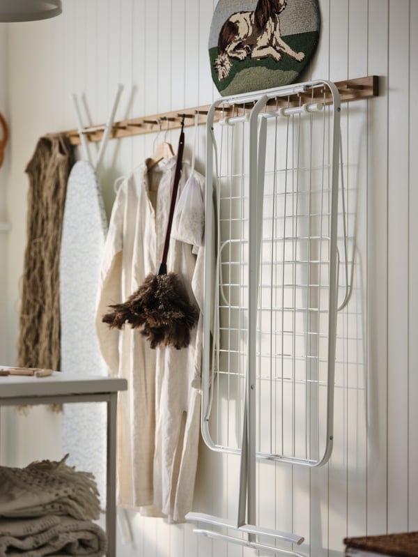 Sur un mur lambrissé de bois, séchoir MULIG et autres accessoires de lessive/nettoyage rangés sur plusieurs patères à 6 boutons HÖVOLM alignées.