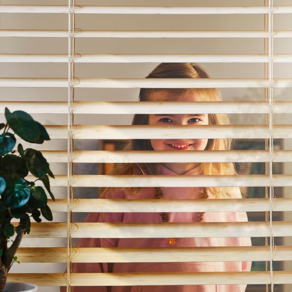 A close-up of a smiling child looking through a VECKLARFLY Venetian blind made from bamboo.