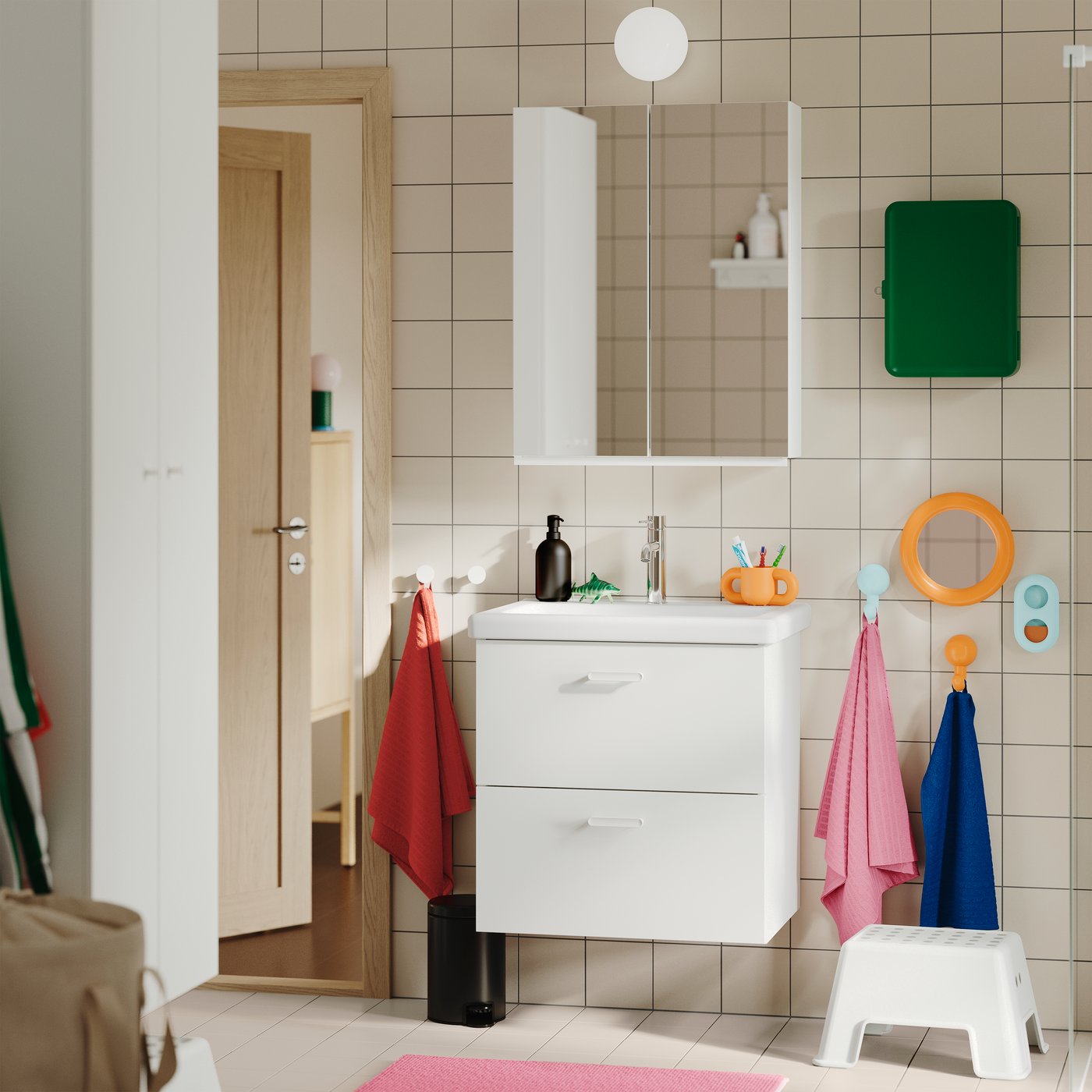 A tiled bathroom featuring the white TVÄLLEN/ENHET wash-stand with two drawers, wall-mounted with colourful towels nearby.