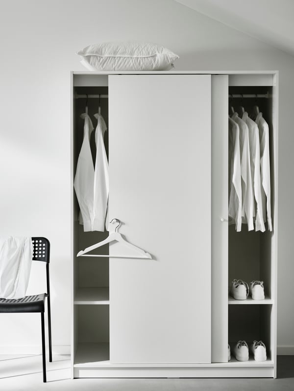 A white IDANÄS wardrobe with a basket on top beside a white IDANÄS open wardrobe, both filled with clothes.