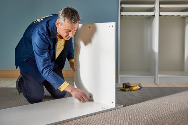 An IKEA staff member is sitting with his knees on the floor, assambling a closet