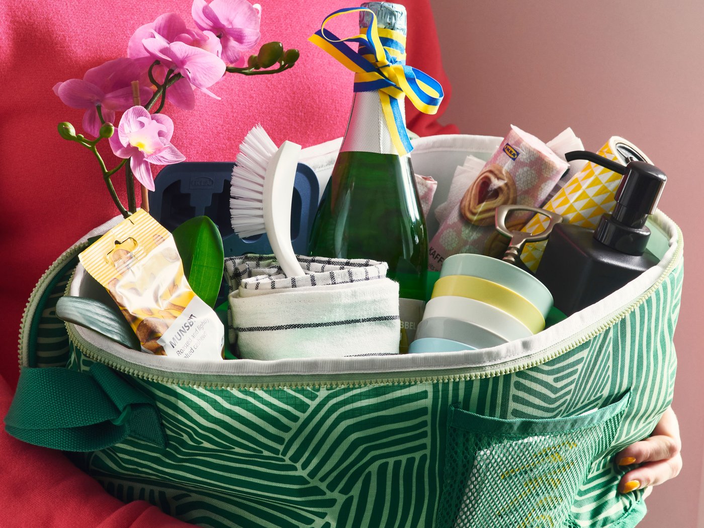 Une personne vêtue d'un pull rose tient un panier vert rempli de friandises.