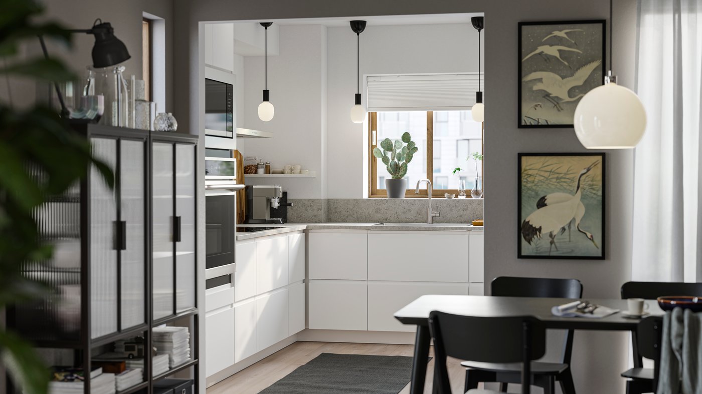 A small kitchen with smooth white VOXTORP fronts, white walls, a gray rug on the floor and three small black pendant lamps.