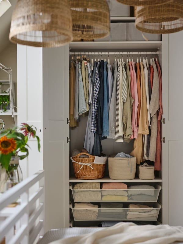 A white PAX GRIMO wardrobe with two doors open showing clothing on rails, in mesh drawers and in baskets on shelves.