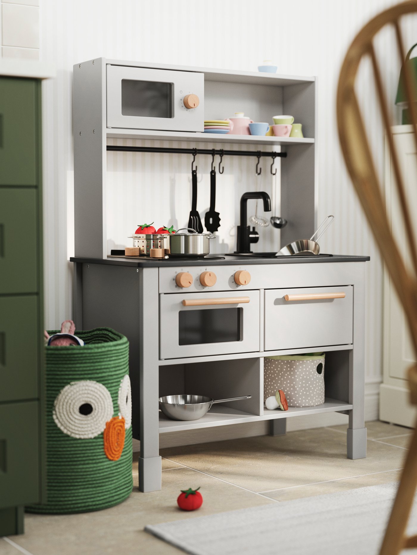 A SILLTRUT kitchen for children with toy pots, pans, and utensils, next to a green woven basket with a playful owl design.