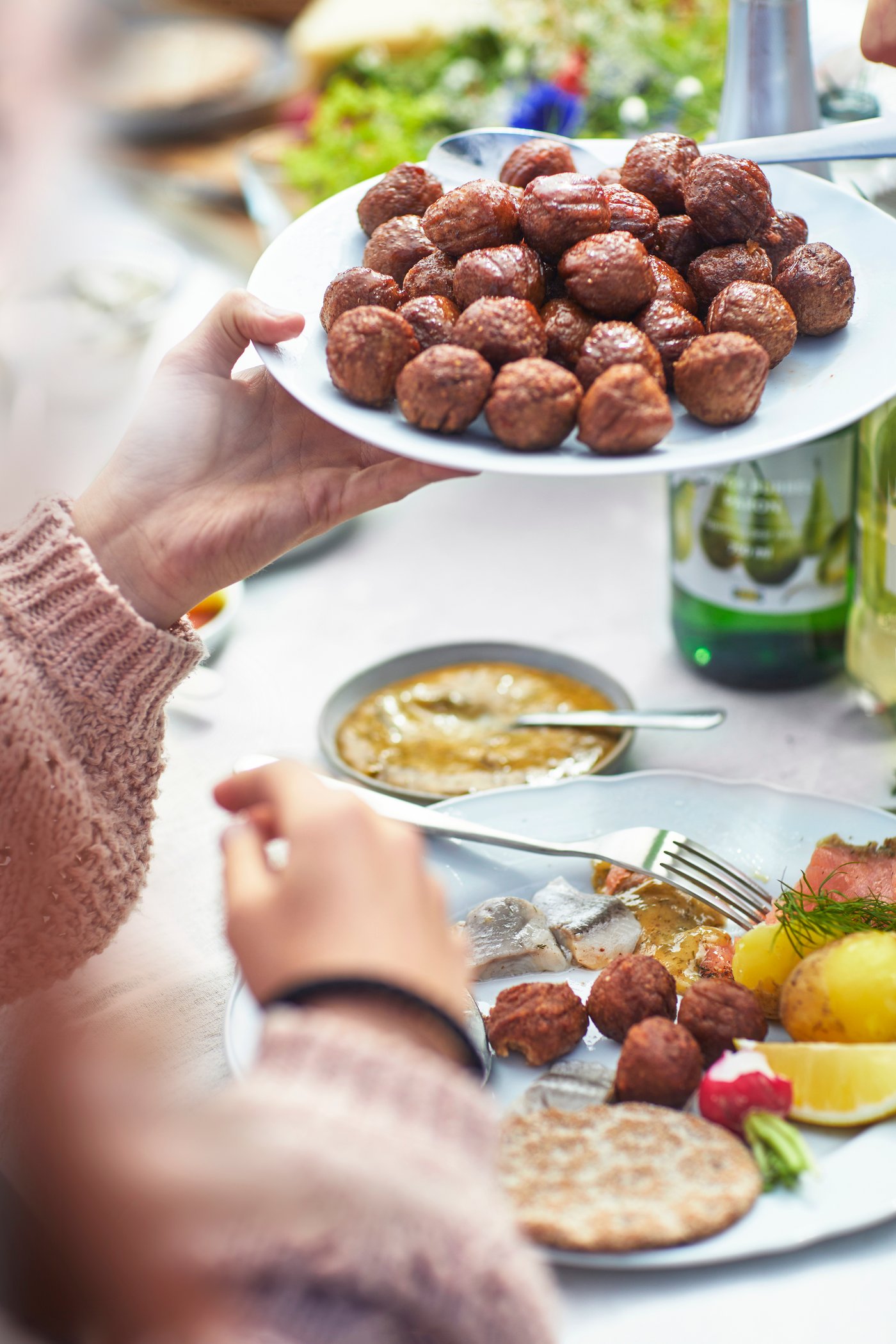 A person passing on a plate of HUVUDROLL plant balls at the table.