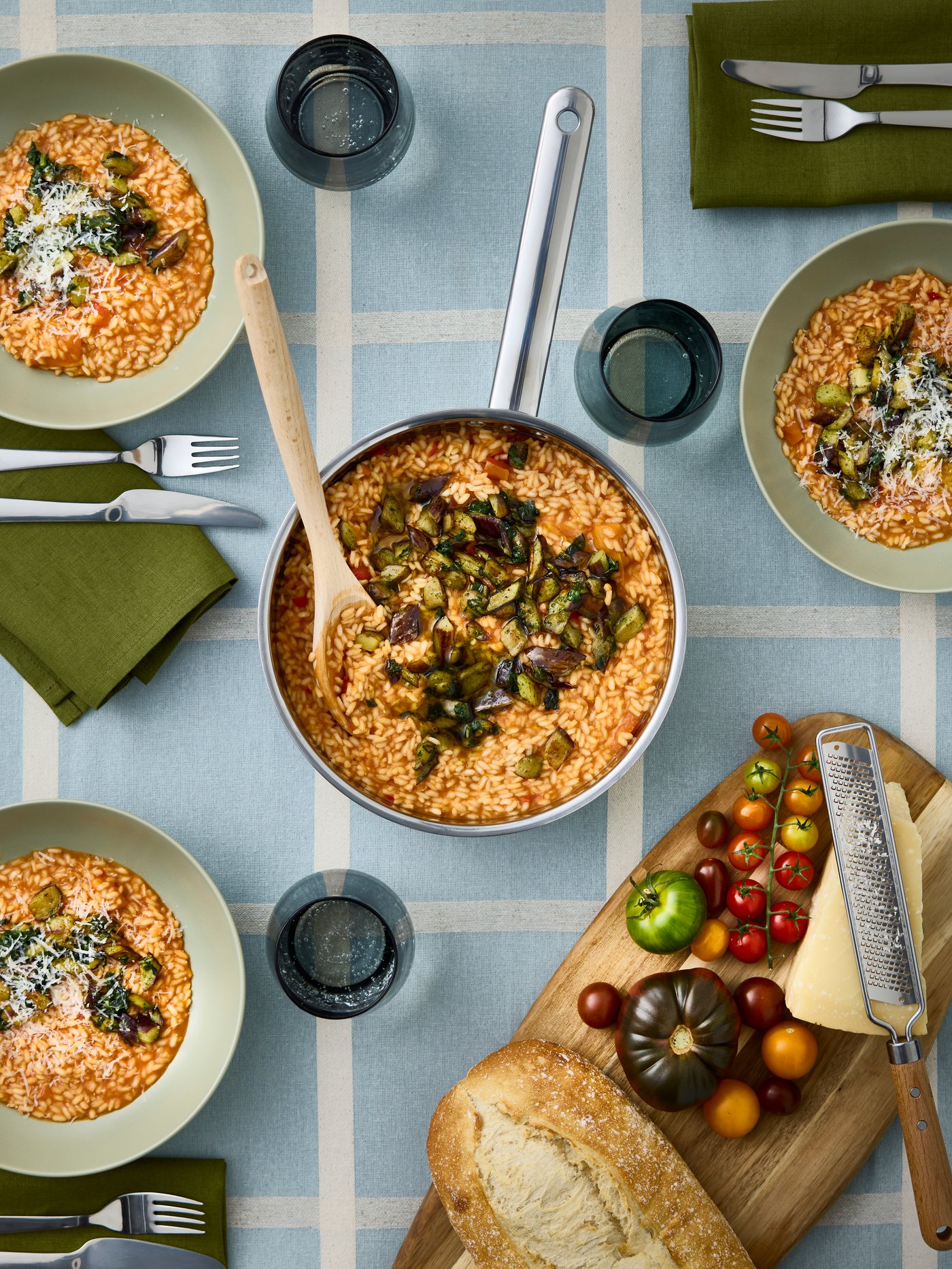 There’s creamy risotto in an IKEA 365+ sauté pan in stainless steel and three FÄRGKLAR deep plates with risotto next to it.