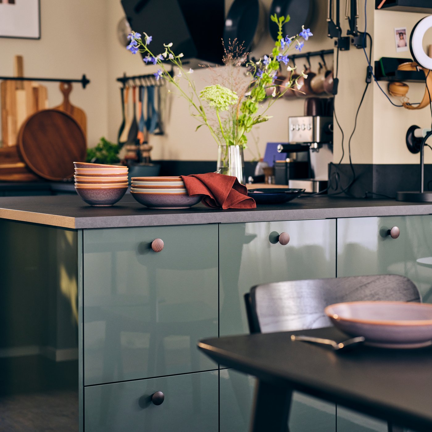 A kitchen with KALLARP high-gloss dark grey green kitchen fronts, EKBACKEN worktop in black laminate, bowls and flowers.