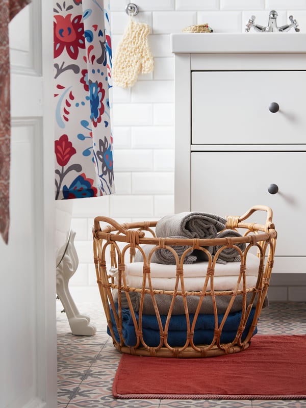 Ein IKEA SNIDAD Korb aus Rattan auf dem Boden des Badezimmers. Er dient hier als Aufbewahrung für frische Handtücher.