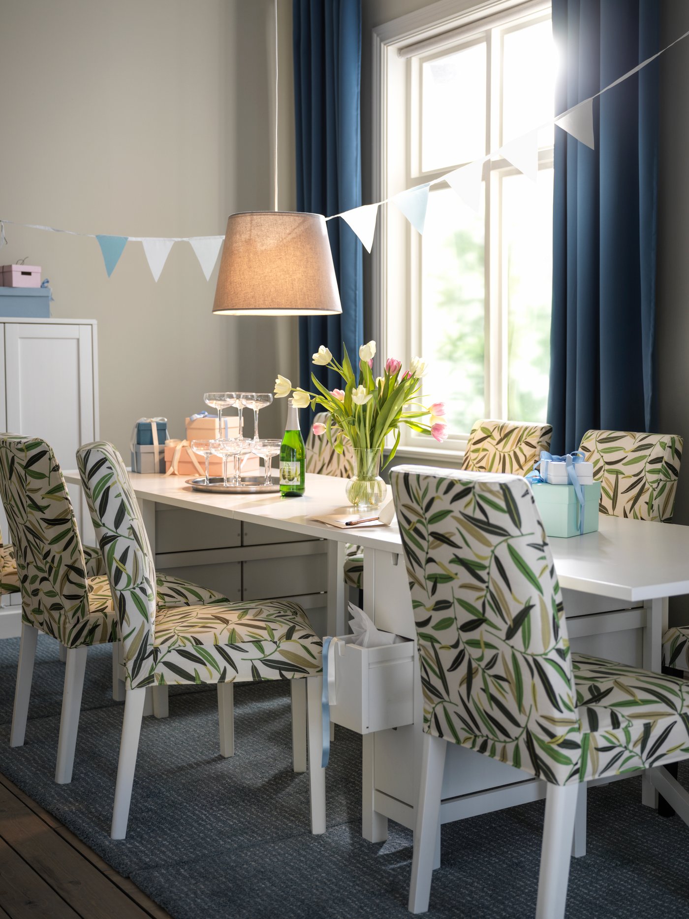 Sillas de comedor BERGMUND color blanco con funda con diseño de hojas multicolor, frente a una mesa abatible blanca.