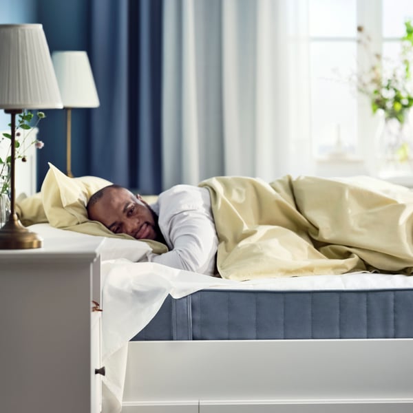 A man lies on an IKEA VESTMARKA pocket sprung mattress that is white on the top and dark grey on the sides.
