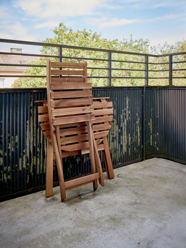 A bare concrete floor on a balcony with ASKHOLMEN chair and table folded and resting against the balcony wall.